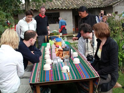 Groep reizigers ontbijt aan lange tafel in Ecuador, met brood, koffie en gekleurde tafelloper.