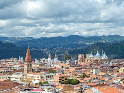 Uitzicht over Cuenca in Ecuador met kathedraal, kerktorens en bergen onder een bewolkte lucht.