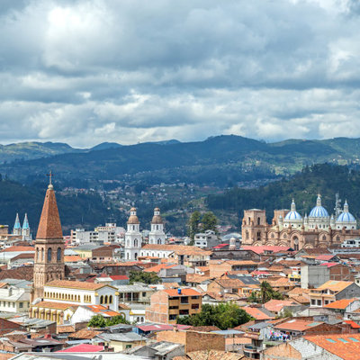 Uitzicht over Cuenca in Ecuador met kathedraal, kerktorens en bergen onder een bewolkte lucht.