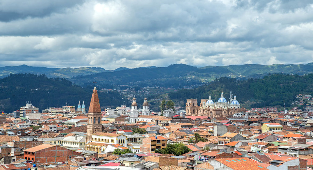 Uitzicht over Cuenca in Ecuador met kathedraal, kerktorens en bergen onder een bewolkte lucht.
