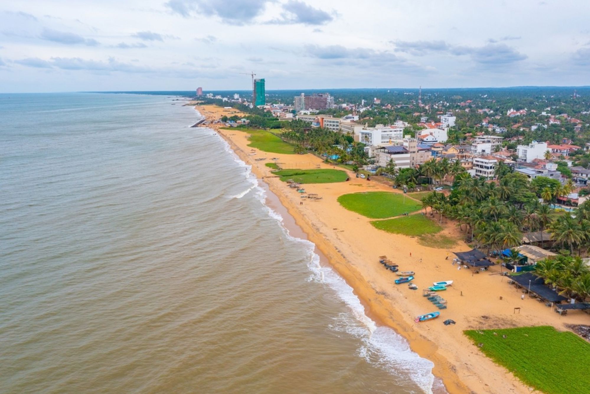 het strand en de kustlijn van Negombo, Sri Lanka, met palmbomen, vissersboten en bebouwing.