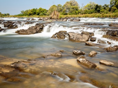Stromende rivier met kleine watervallen en rotsen, op de route van Victoria Falls naar Kaapstad.