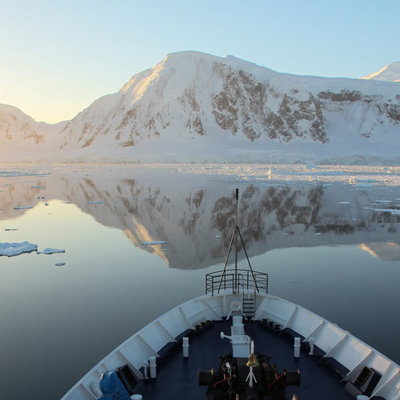 Boeg van expeditieschip vaart door rustig ijswater langs besneeuwde bergen in Antarctica tijdens groepsrondreis.