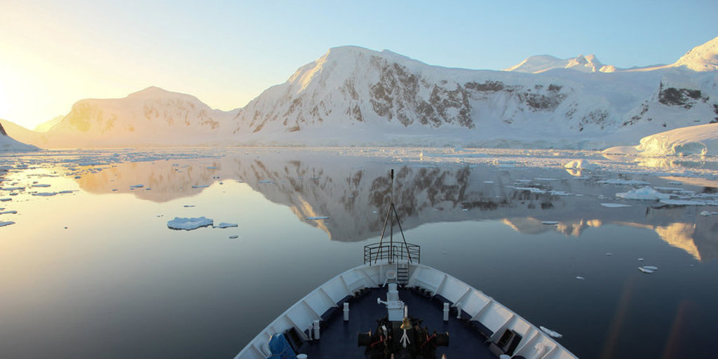 Boeg van expeditieschip vaart door rustig ijswater langs besneeuwde bergen in Antarctica tijdens groepsrondreis.