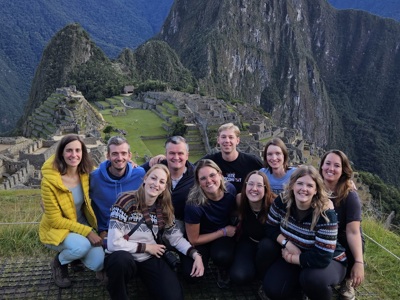 22-35ers groepsreis bij Machu Picchu in Peru, met de ruïnes en Huayna Picchu op de achtergrond.