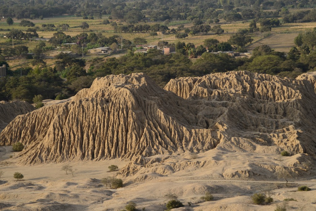 Erosielandschap bij de piramides van Túcume in Noord-Peru, met akkers en dorp op de achtergrond.