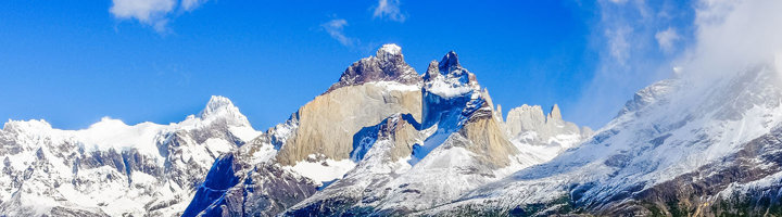 Besneeuwde bergtoppen van het Torres del Paine-massief in Patagonië onder een heldere blauwe lucht.