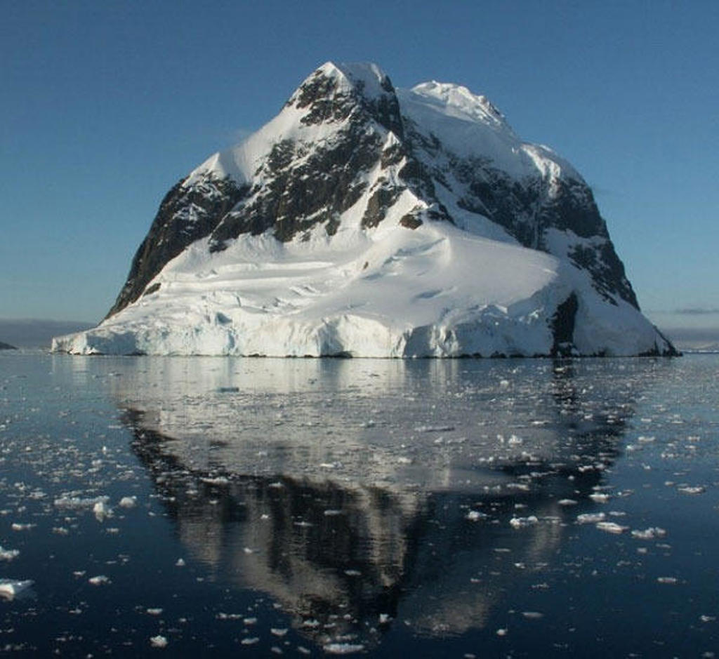 Besneeuwde berg in Antarctica weerspiegeld in kalm zeewater met drijfijs.