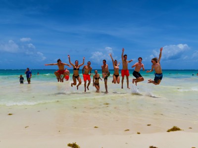 Familiegroep springt in de branding op een wit zandstrand aan de Caribische kust van Mexico.