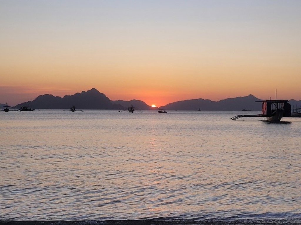 Zonsondergang boven zee met eilandjes en een boot, tijdens groepsrondreis Filipijnen.