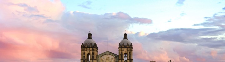 Santo Domingo de Guzmán-kerk in Oaxaca bij zonsondergang, met bergen op de achtergrond.