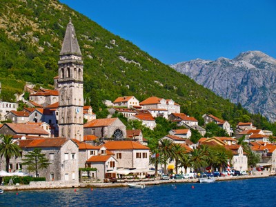 Kustplaats in de Balkan met stenen huizen, kerktoren en bergen aan zee tijdens de Route Balkan fietsvakantie.