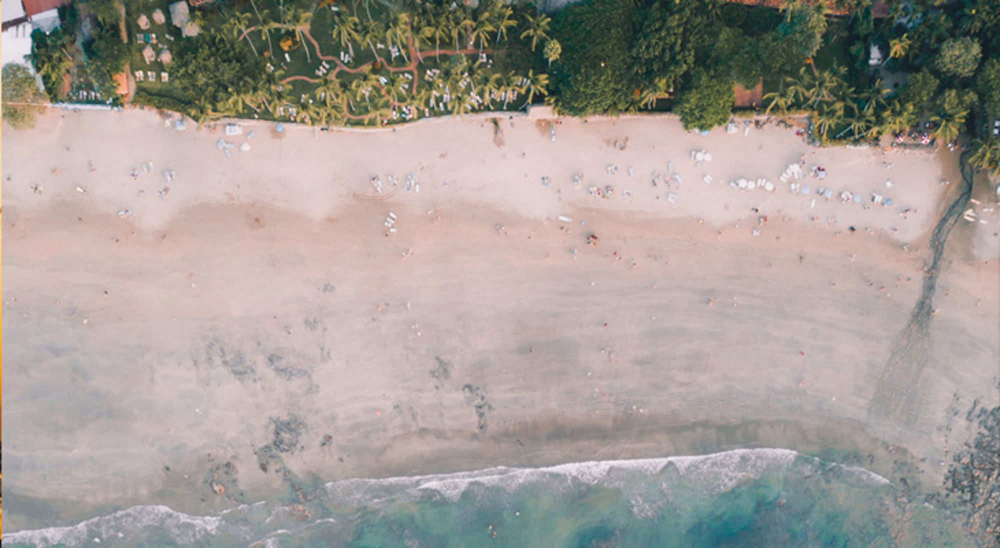 een breed zandstrand met palmbomen en strandgangers aan de kust van Costa Rica.