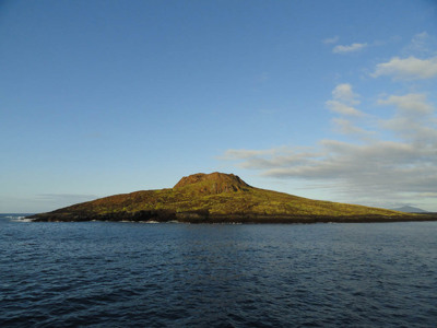 Vulkanisch eilandlandschap in de Galapagoseilanden, gezien vanaf zee onder een helderblauwe lucht.