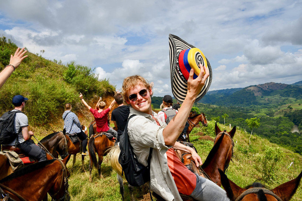 22-35ers te paard in de Colombiaanse bergen tijdens rondreis, met reiziger die een sombrero omhoog houdt.