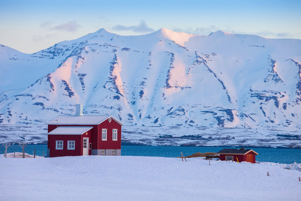 Rood huis in een besneeuwd landschap aan zee, met besneeuwde bergen op de achtergrond in Noord-IJsland.