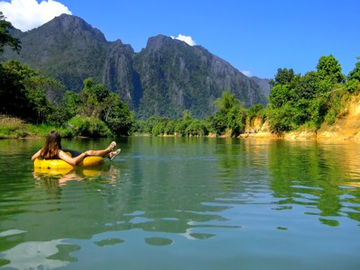Vrouw drijft op een rubberband op een rivier met groene bergen op de achtergrond in Laos.