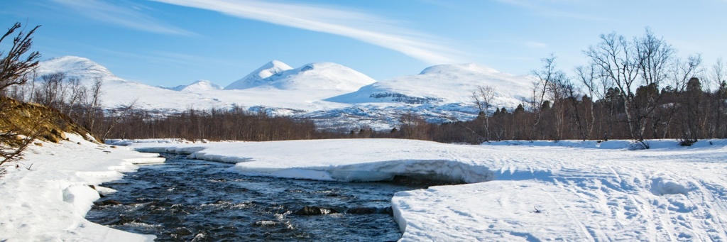 Sneeuwlandschap met rivier en besneeuwde bergen in Zweeds en Noors Lapland.