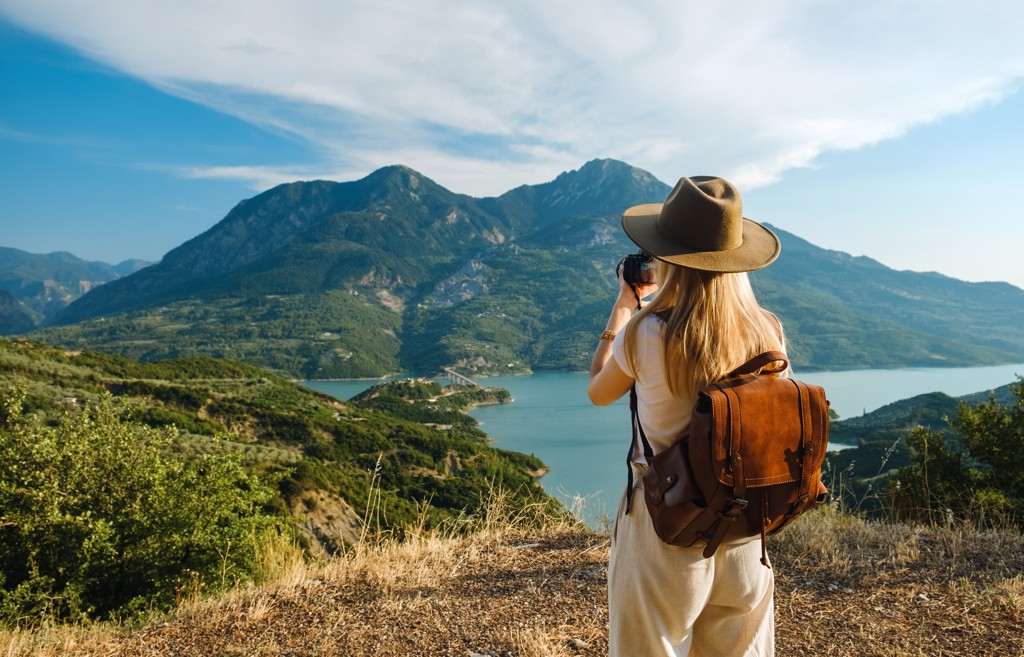 Jonge reiziger met rugzak fotografeert bergen en een meer tijdens 22-35ers reis in Griekenland.