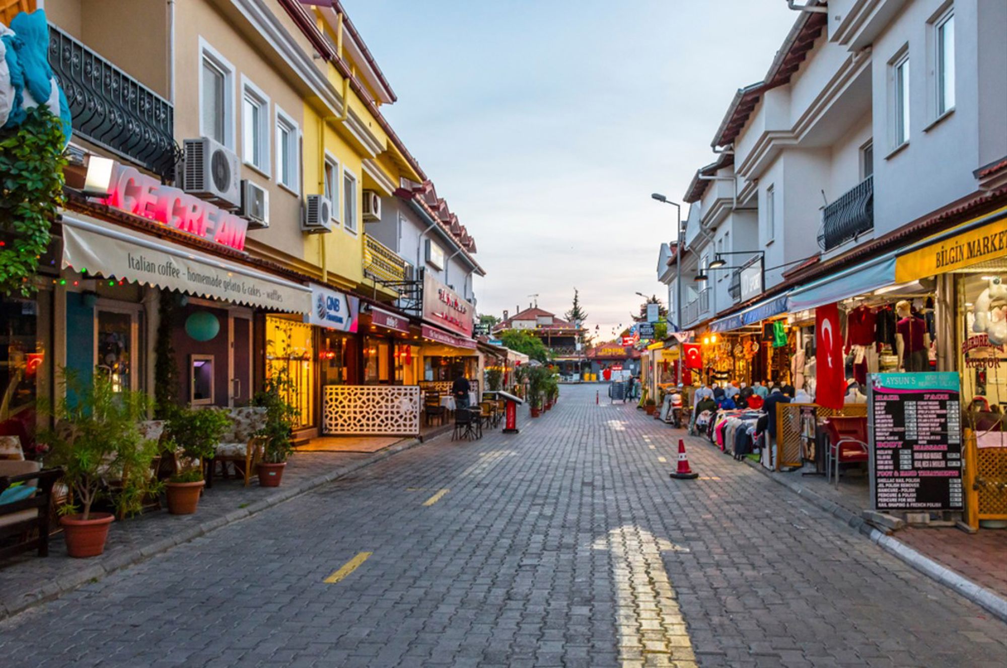 Winkelstraat met winkeltjes, restaurants en Turkse vlaggen in een badplaats in Turkije bij zonsondergang.