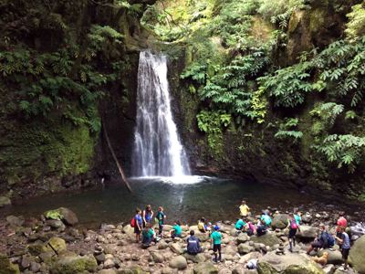 Waterval in weelderig groen ravijn op São Miguel, Azoren, met wandelaars bij de rotsige oever.