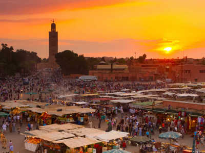 Zonsondergang boven het Djemaa el Fna-plein in Marrakech met marktstalletjes en de Koutoubia-moskee.