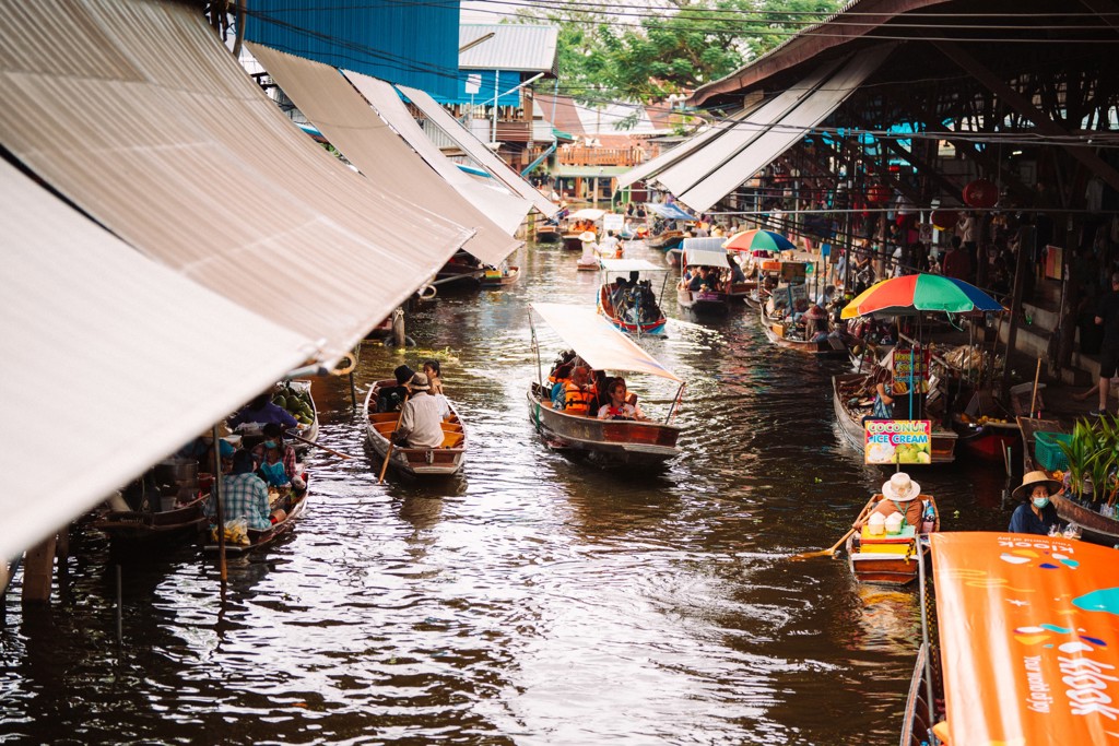 Drijvende markt in Thailand met bootjes vol koopwaar en kleurrijke parasols tijdens een familiereis.