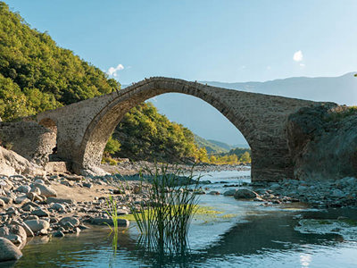 Oude stenen boogbrug over een rivier in een groene vallei op de route door Albanië, Kosovo en Noord-Macedonië.