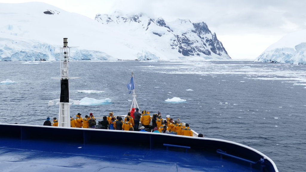 Expeditieschip met passagiers bij ijsbergen en besneeuwde bergen tijdens groepsrondreis Antarctica.