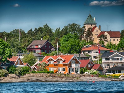Kleurrijke houten huizen aan de kust in Scandinavië, met een kasteel op de heuvel erachter.