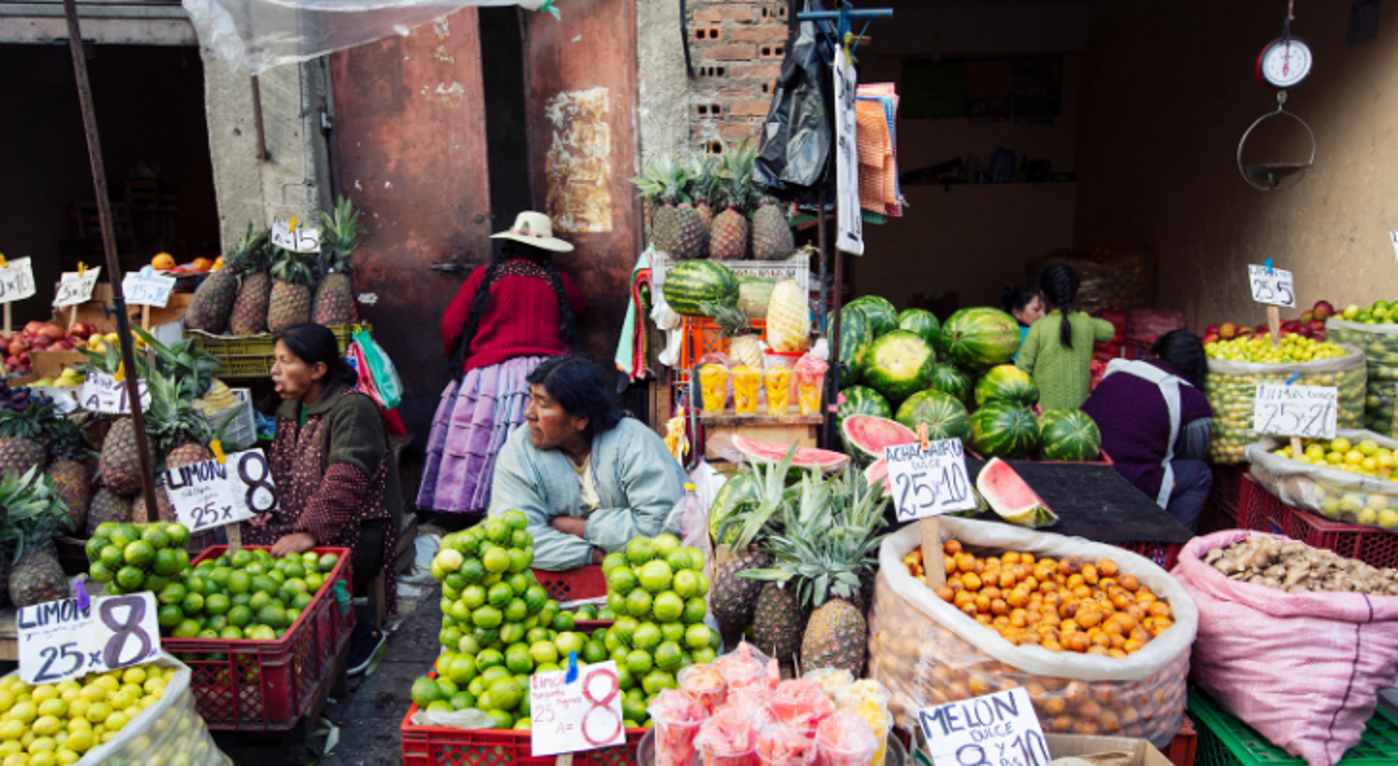 Fruitmarkt in Bolivia met verkopers en stapels ananas, watermeloenen, limoenen en sinaasappels.