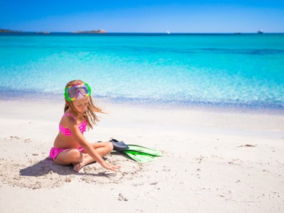 Kind met snorkelbril en zwemvliezen speelt op wit zandstrand aan turquoise zee in Mexico.