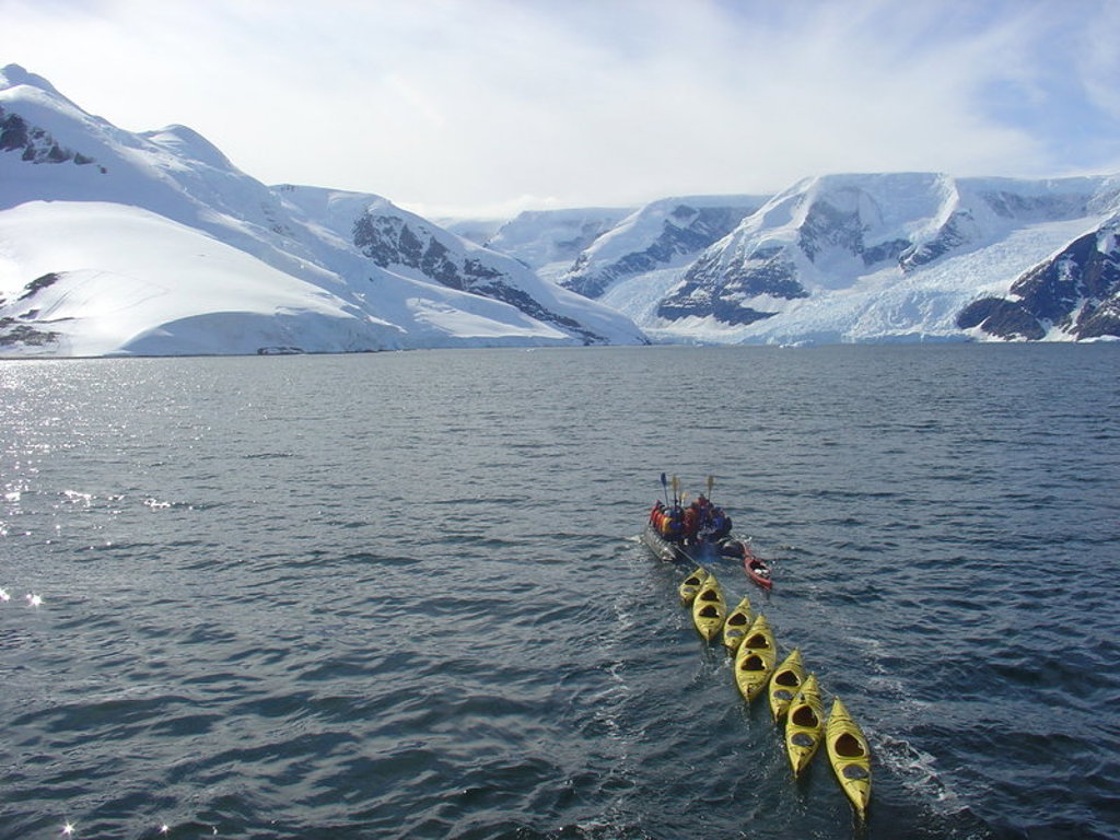 Zodiacboot met kajaks op zee bij besneeuwde bergen in Antarctica tijdens een groepsrondreis.