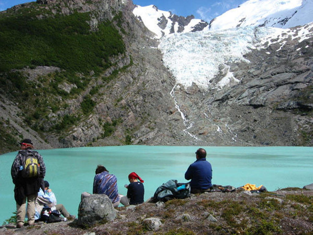 Wandelaars rusten aan een turquoise gletsjermeer met krakende gletsjer op de achtergrond in Patagonië.