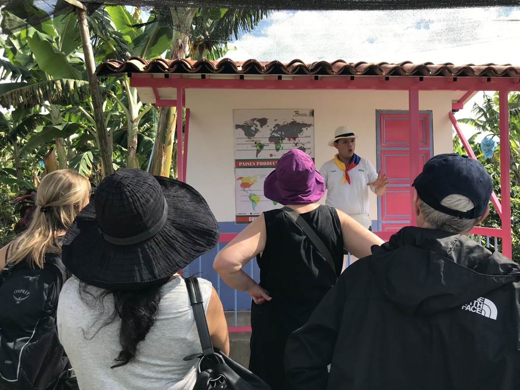 Rondleiding op een koffieplantage in Colombia tijdens een groepsrondreis, met gids en reizigers bij een kleurrijk huisje.