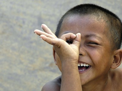 Lachend kind kijkt door een handcirkel, reisroute Laos & Cambodja.