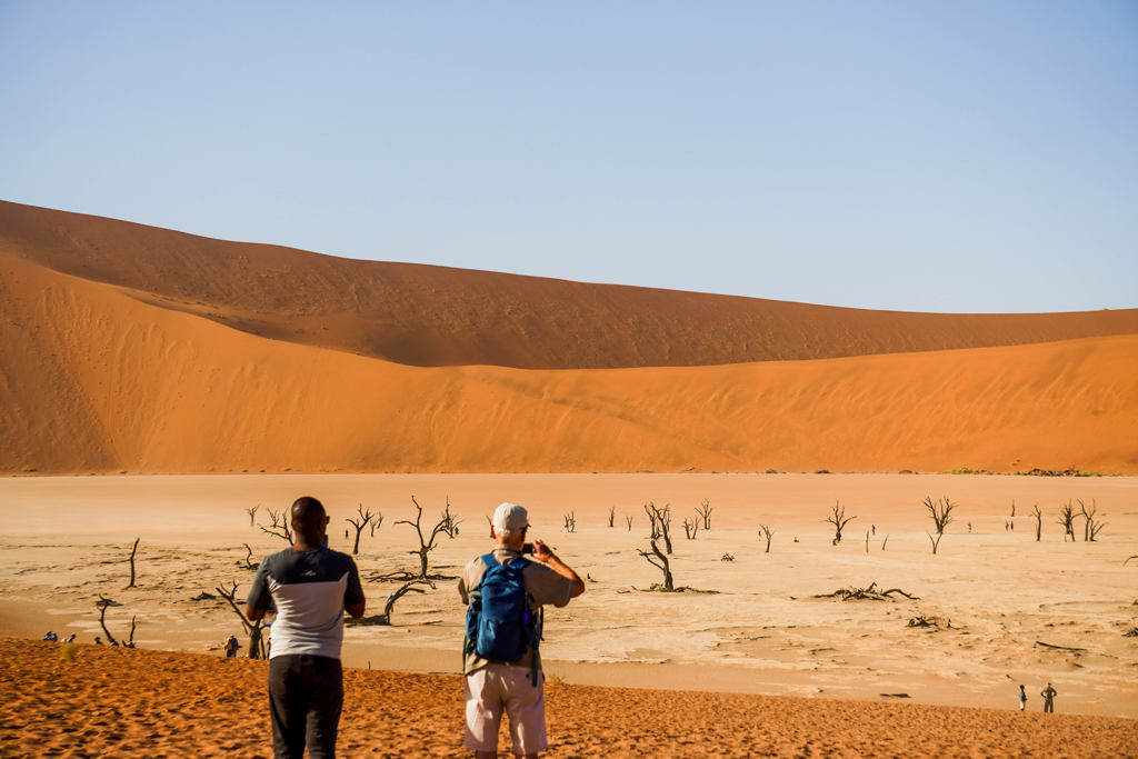 Reizigers kijken uit over Deadvlei met dode bomen en rode zandduinen in Namibië tijdens een kampeerreis door Zuidelijk Afrika.