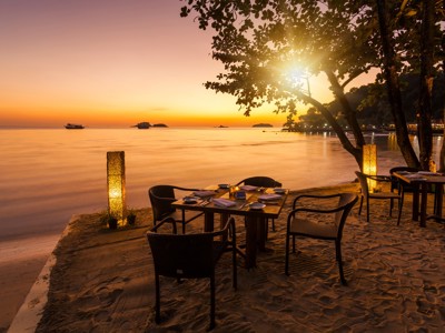 Diner aan het strand bij zonsondergang in Thailand, met gedekte tafels en uitzicht op zee.