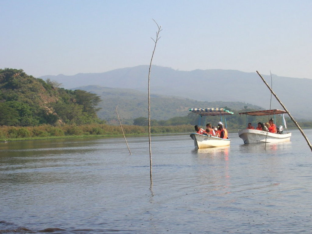Boottocht met familie over een rivier in Kenia, met groene oevers en bergen op de achtergrond.