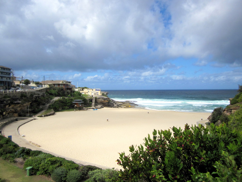 Zandstrand en ruige kust bij Sydney, Australië, met golven en bewolkte lucht tijdens een groepsrondreis.