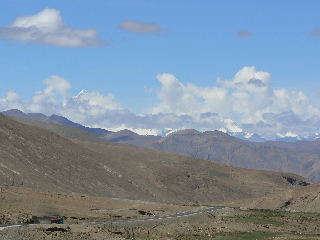 Berglandschap in Tibet met kronkelende weg en besneeuwde Himalaya-toppen onder een blauwe lucht.