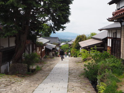Traditionele straat in Japan met stenen pad, houten huizen en uitzicht op groene heuvels.