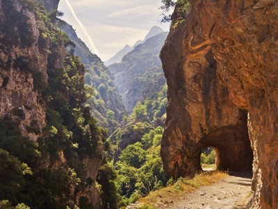 Wandelpad langs rotswand met tunnel en uitzicht op de Picos de Europa in Spanje.