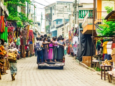 Drukke marktstraat in Guatemala met kleurrijke kraampjes en mensen achterop een pick-up.