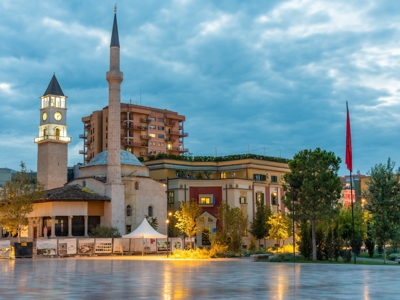 Skanderbegplein in Tirana met Et’hem Bey-moskee, klokkentoren en Albanese vlag bij avondlicht.