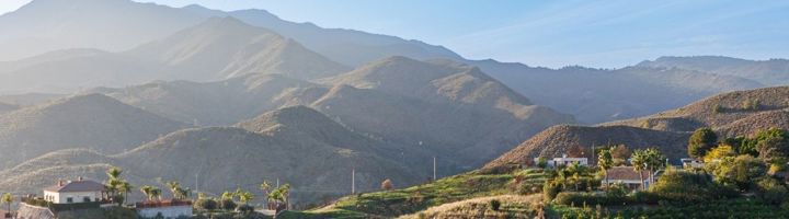 Panoramisch uitzicht op het berglandschap van Andalusië in Zuid-Spanje, met heuvels, dorpjes en palmbomen.