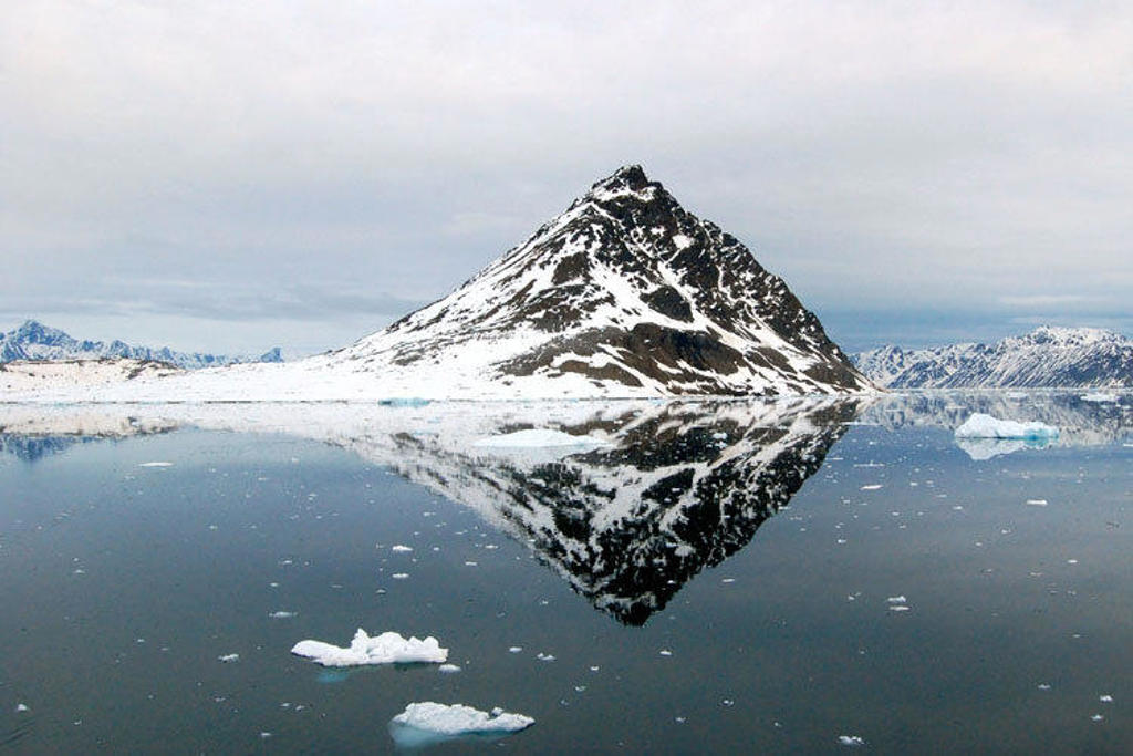 Besneeuwde berg op Spitsbergen weerspiegeld in stille fjord met drijvend ijs tijdens groepsrondreis.