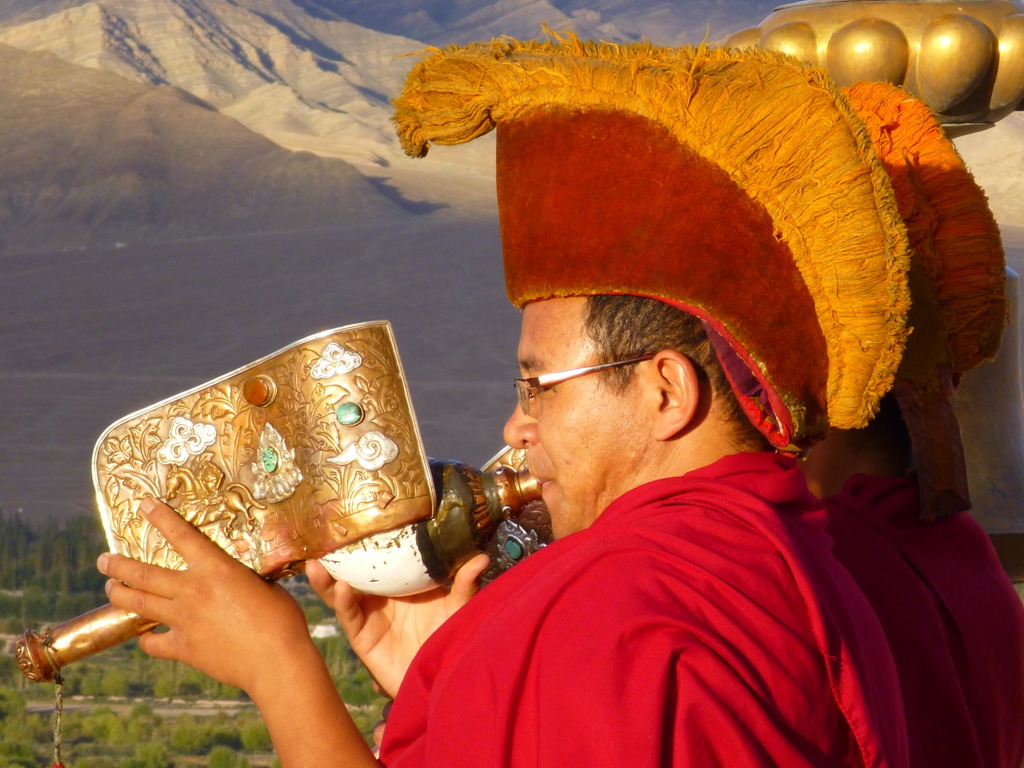 Boeddhistische monnik blaast op ceremoniële hoorn met Himalaya-bergen op de achtergrond in Ladakh, India.