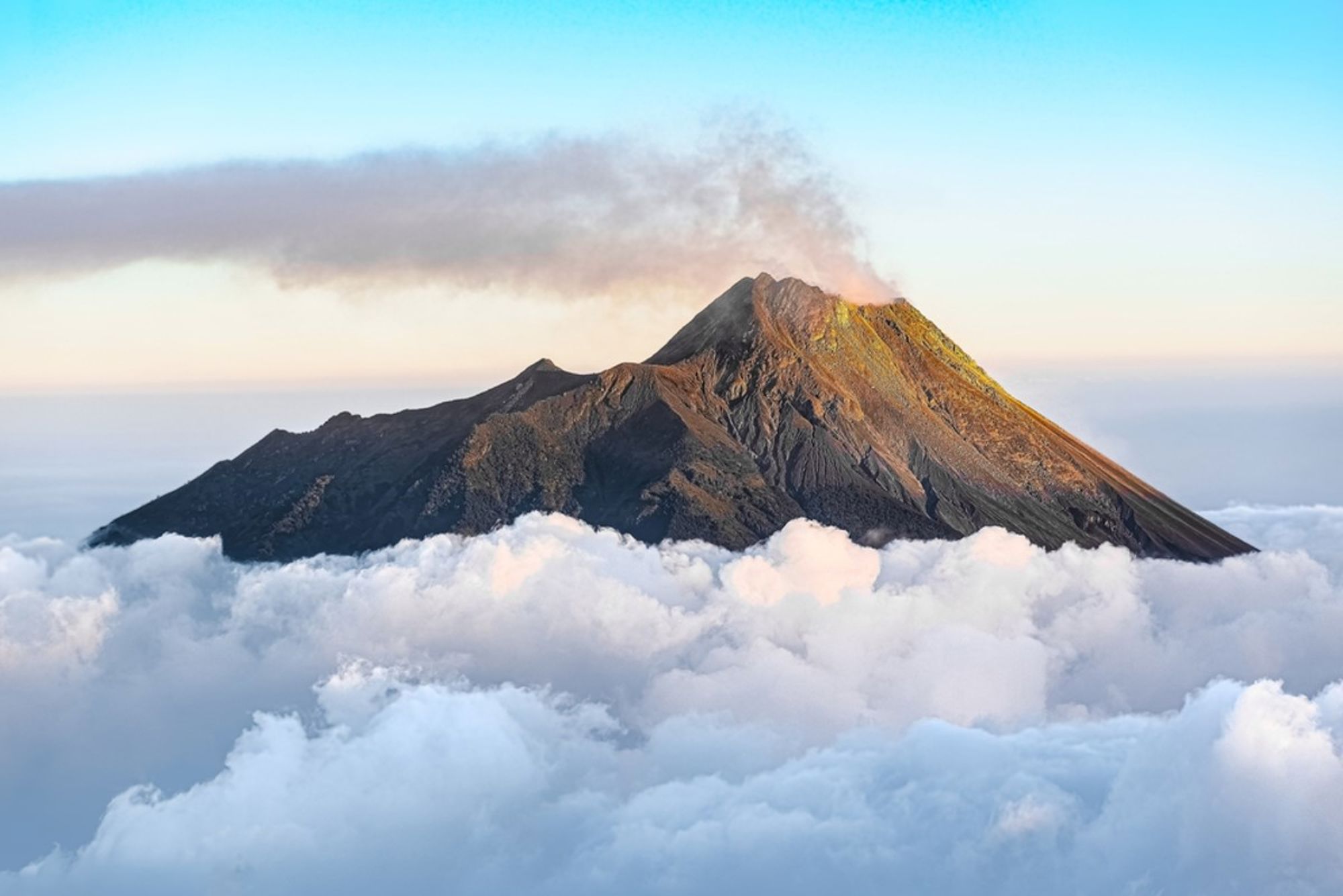 Rokende vulkaantop bij zonsopkomst boven een wolkendek in Indonesië.