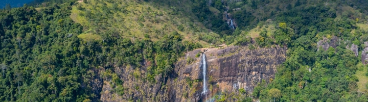 Diyaluma Falls waterval in Sri Lanka, met water dat langs een hoge rotswand in groen berglandschap stroomt.